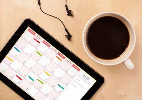 Tablet pc showing calendar on screen with a cup of coffee on a d