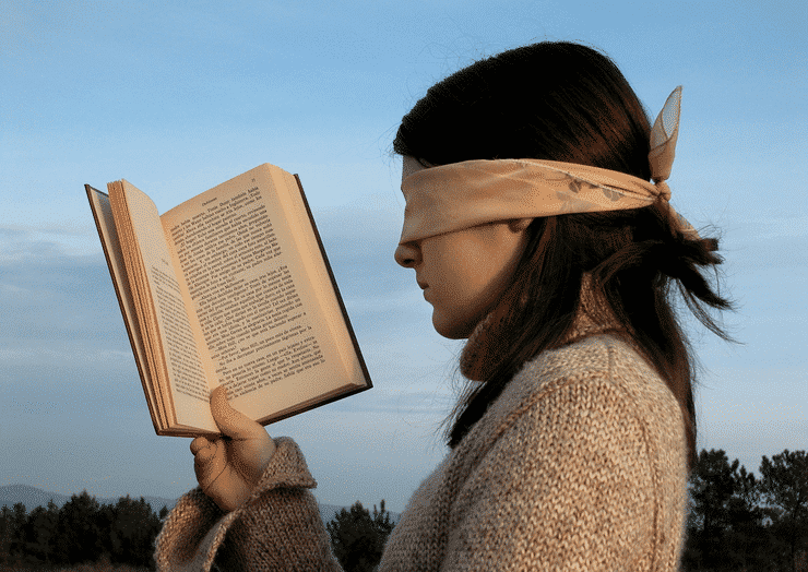 Woman trying to read book whilst blindfolded